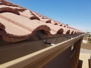 Up-close look of a seamless k-style aluminum rain gutter 6 inches attached to a house with a red brick roof.
