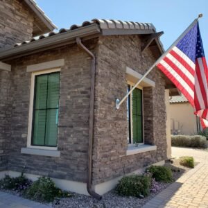 The front of a brick house with an American flag hung up, and one 10ft piece seamless K-Style rain gutter with one brown downspout.