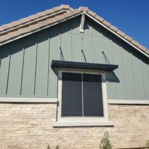 A view of the front of a house with one window with one awning right above it and a black outdoor sun screen covering the window.